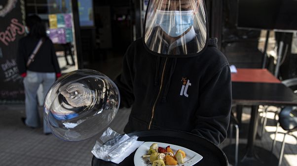Un camarero con mascarilla y visera de protección sirve un plato en Santiago de Chile Un camarero con mascarilla y visera de protección sirve un plato en Santiago de Chile