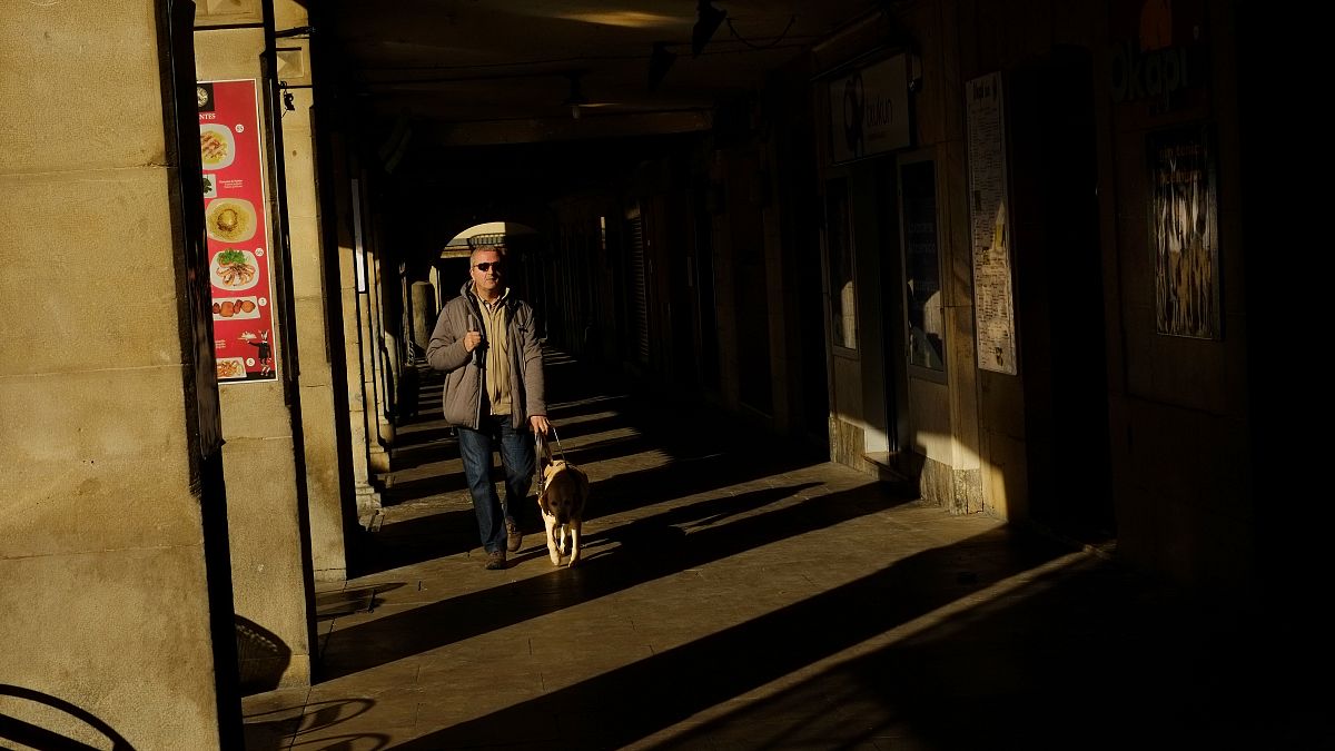 Un hombre invidente pasea con su perro guía por los pórticos de la ciudad vieja durante un día de invierno en Pamplona, en el norte de España. 