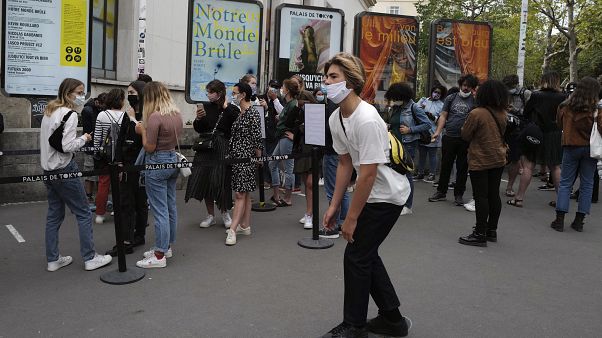 Un joven pasa en monopatín ante la gente que hace cola ante el Palacio de Tokio en París Un joven pasa en monopatín ante la gente que hace cola ante el Palacio de Tokio en París