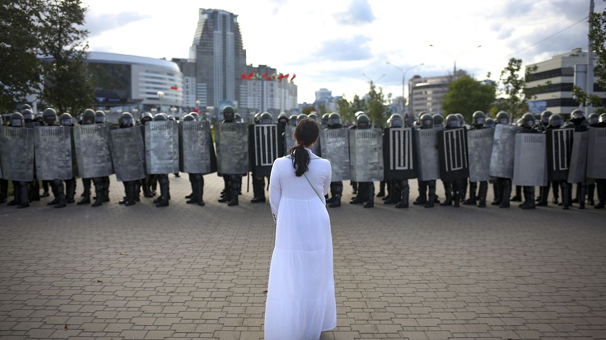 Женщина в белом платье перед шеренгой силовиков в Минске