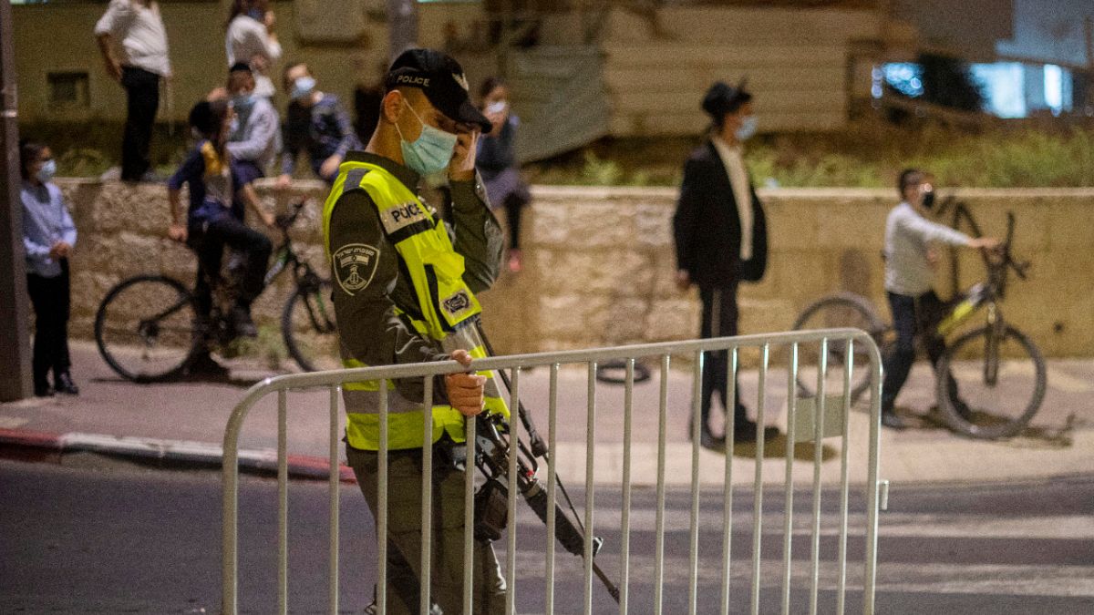 In this Tuesday, Sept. 8, 2020 file photo, an Israeli border policeman sets up a barrier during an overnight curfew amid the coronavirus pandemic, Beit Shemes, Israel.
