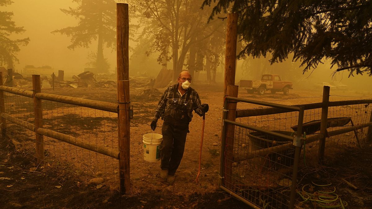 George Coble carries a bucket of water to put out a tree still smoldering on his property destroyed by a wildfire Saturday, Sept. 12, 2020, in Mill City, Ore. 