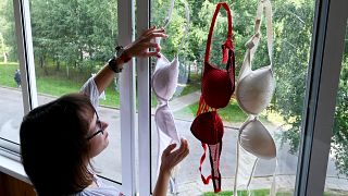A woman hangs red and white bras in a window