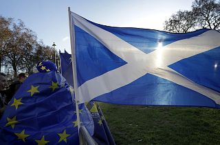 A demonstrator wearing a European Union flag stands with the flag of Scotland near parliament in London.