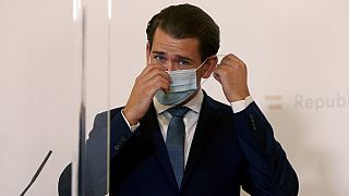 Austrian Chancellor Sebastian Kurz adjusts his face mask, standing behind two plexiglass shields during a press conference at the federal chancellery in Vienna, Austria