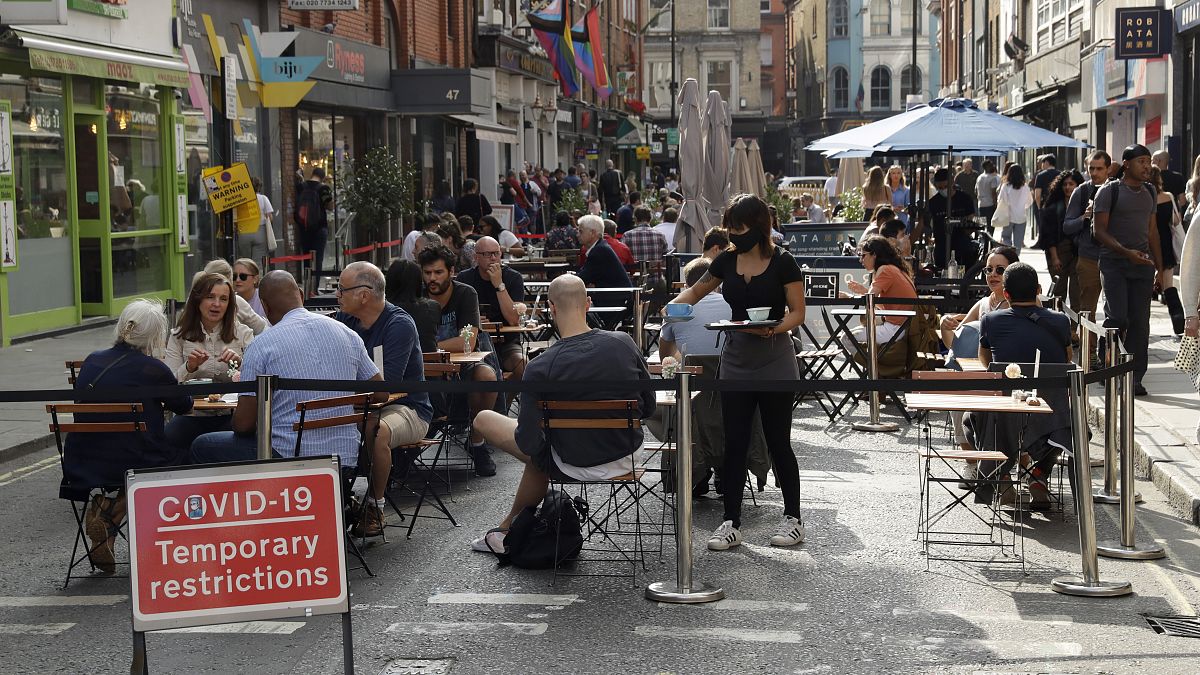 People sit outside on a street closed to traffic to try to reduce the spread of coronavirus in London, Saturday, Sept. 19, 2020.