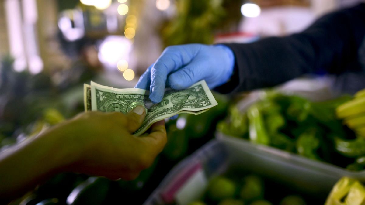  Owner of a fruit and vegetables stand, wears gloves as he exchanges cash with a customer