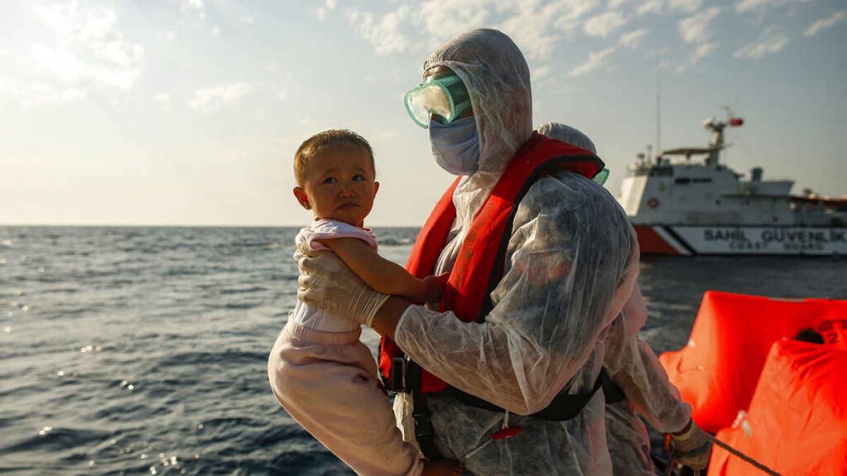 A Turkish coast guard officer, wearing protective gear to help prevent the spread of coronavirus, carries a child off a life raft during a rescue operation in the Aegean Sea, 