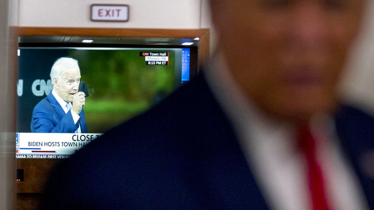 A television screen shows Democratic presidential candidate Joe Biden holding up a mask, as President Donald Trump talks with reporters.