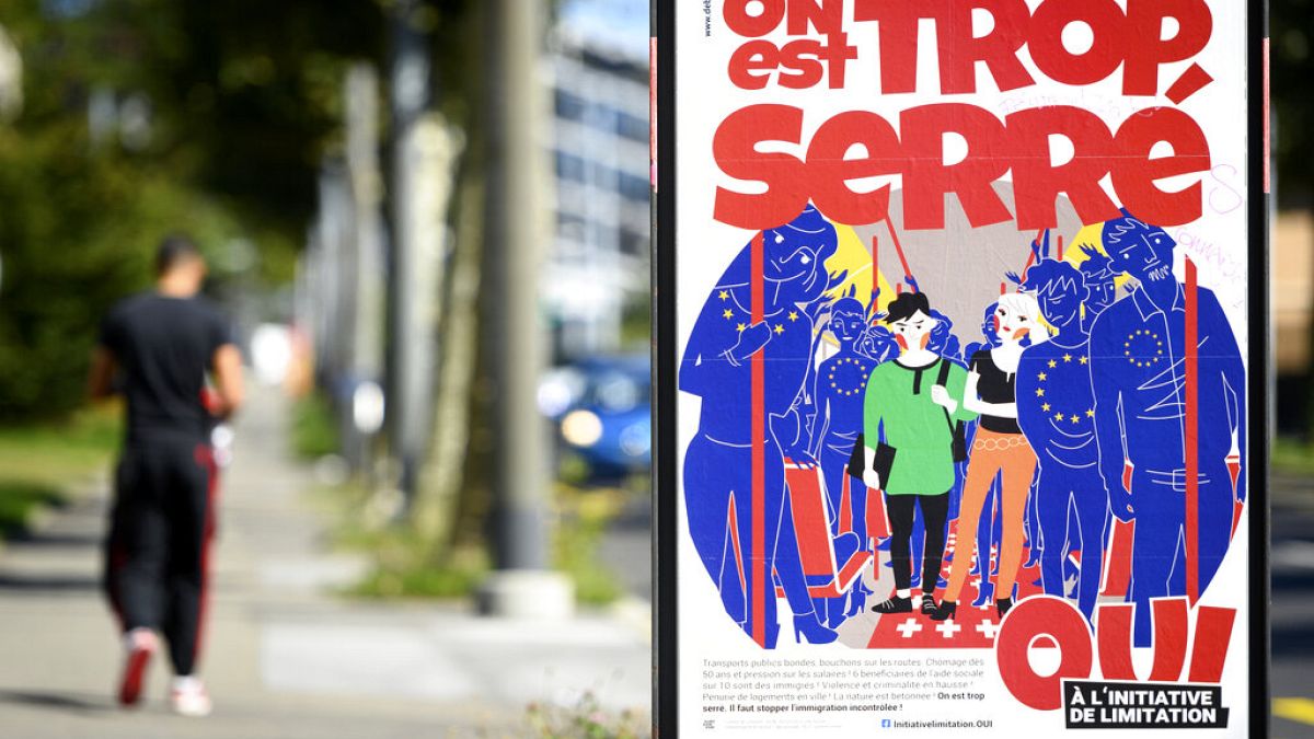 A poster of the Swiss People's Party (SVP) for a moderate immigration initiative reading 'we're too tight!' is displayed in a street in Lausanne