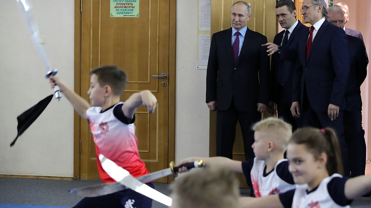 Russian President Vladimir Putin, background left, watches a performance by students of the Martial Arts Centre