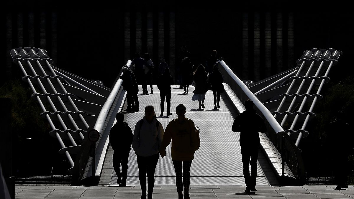 People are silhouetted as they walk over Millennium Bridge in London