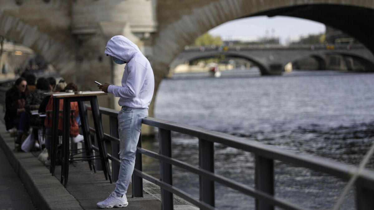 A man check his phone at a cafe terrace along the Seine river, Saturday Sept.26, 2020 in Paris.