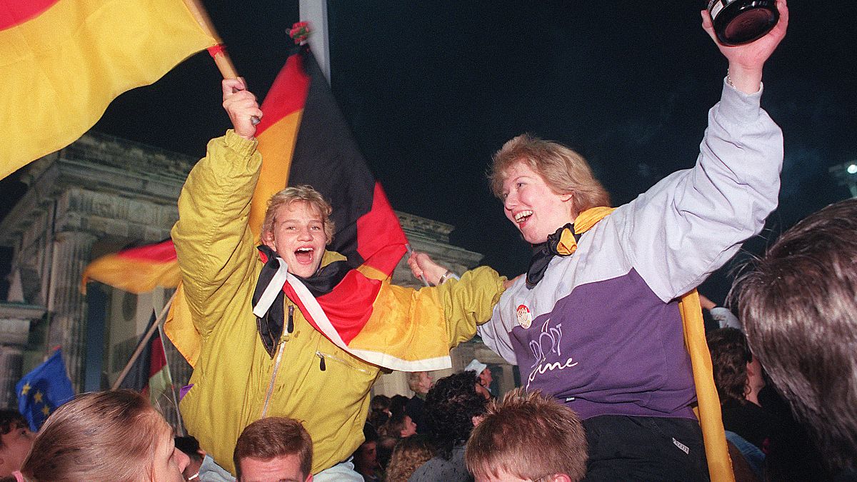 Jóvenes berlinesas ondean banderas alemanas durante la celebración de la reunificación del país en la Puerta de Brandenburgo, Berlín. 3 de octubre de 1990