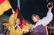 Берлинская молодежь размахивает немецкими флагами, празднуя воссоединение страны у Бранденбургских ворот. 3 октября 1990 года.