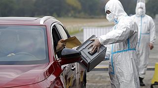 An election committee member, wearing a protective suit, holds a ballot box for a man to vote in regional and senate elections at a drive-in polling station in Prague.