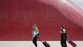 Two women wearing face masks pull their suitcases outside Lisbon's airport, Friday, Sept. 11, 2020