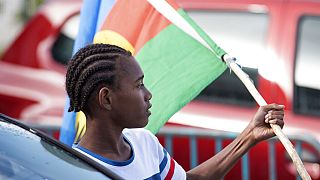 An Independence supporter holds the Kanak flag outside a voting station in the Riviere Salee district of Noumea, New Caledonia, Sunday, Oct.4, 2020