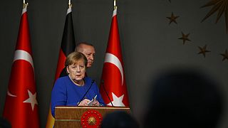 Germany's Chancellor Angela Merkel, left, stands as Turkey's President Recep Tayyip Erdogan, walks behind her