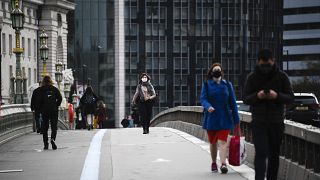 People wearing face masks walk across Westminster Bridge, in London, Wednesday, Oct. 7, 2020.