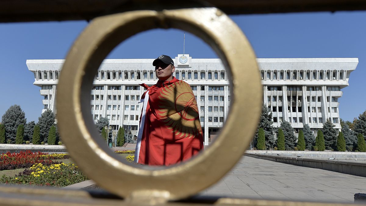 Мужчина с национальным флагом у здания правительства Киргизии