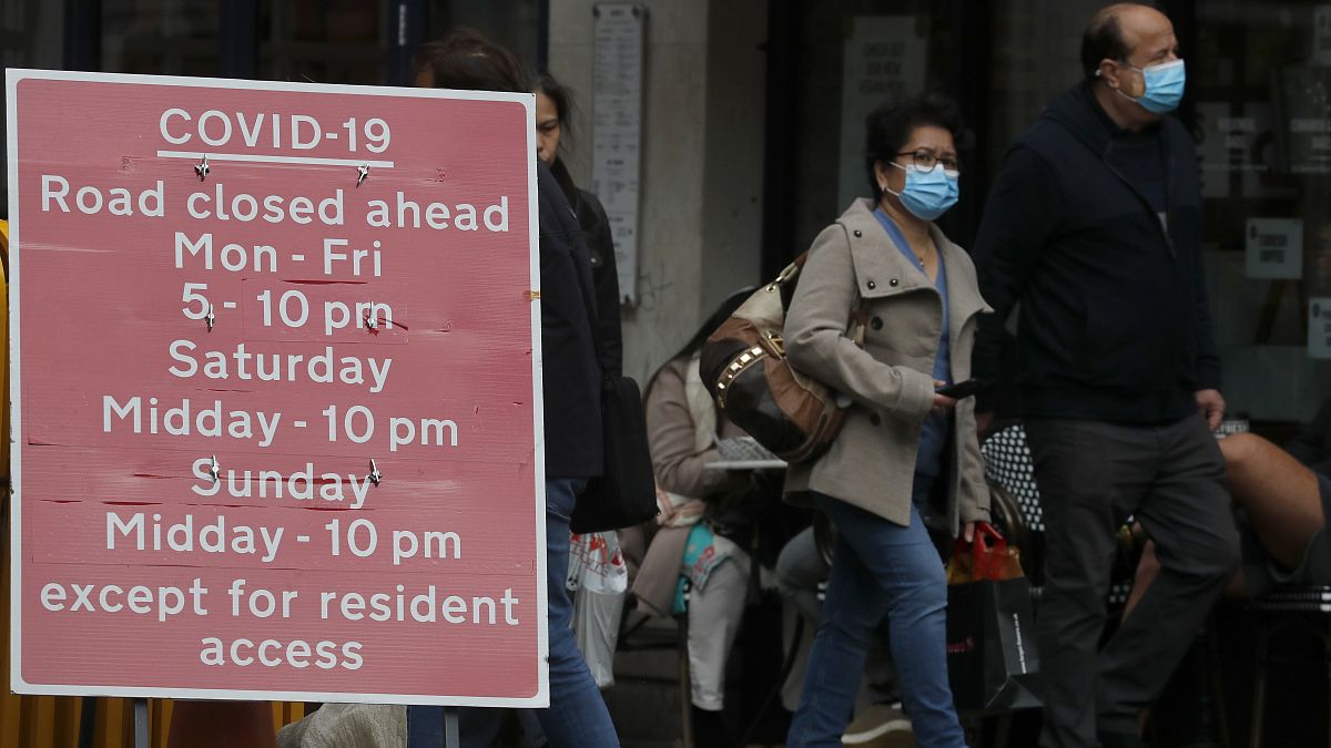 People walk past a sign that refers to COVID-19 closures in London, Friday, Oct. 9, 2020.
