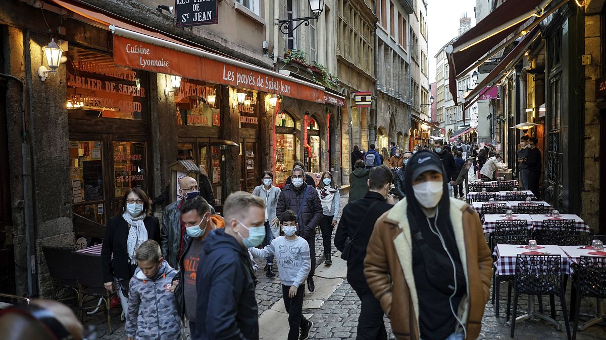 People wearing masks pass by restaurants in Lyon, central France, Saturday, Oct. 10, 2020.
