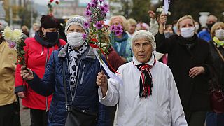 Elderly women hold flowers during an opposition rally to protest the official presidential election results in Minsk, Belarus, Monday, Oct. 12, 2020.