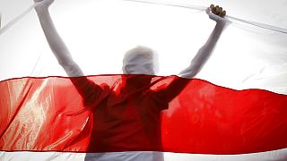 Demonstrator is silhouetted by an old Belarusian national flag during a rally in Minsk, Belarus, Sunday, Oct. 4, 2020