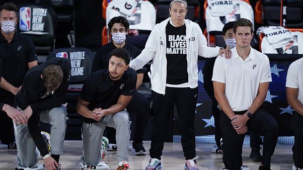 Assistenztrainerin Becky Hammon mit knieenden Spielern der San Antonio Spurs vor einem Match gegen die Memphis Grizzlies im August 2020 Assistenztrainerin Becky Hammon mit knieenden Spielern der San Antonio Spurs vor einem Match gegen die Memphis Grizzlies im August 2020