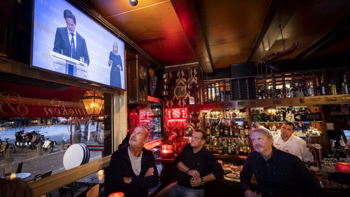 Egy kávézó dolgozói nézik Mark Rutte holland miniszterelnök bejelentését a szigorításokról