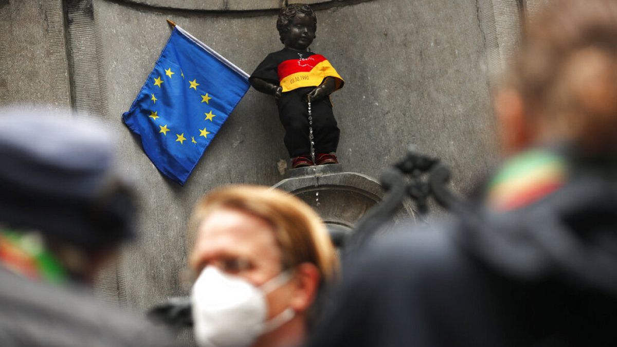 People take photographs of Manneken Pis landmark dressed in the colours of the German flag next to an EU flag in downtown Brussels