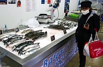 file photo, a woman wearing a face mask buys fish