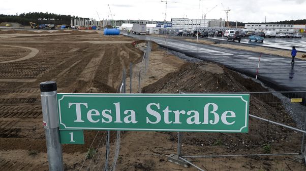 a street sign reading 'Tesla Street 1' stand in front of the construction site of the electric car Tesla Gigafactory in Gruenheide near in Berlin, Germany. a street sign reading 'Tesla Street 1' stand in front of the construction site of the electric car Tesla Gigafactory in Gruenheide near in Berlin, Germany.