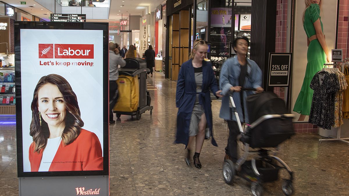 Jacinda Ardern munkáspárti politikus plakátja mellett halad egy pár egy Christchurch-i bevásárlóközpontban
