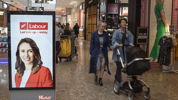 Jacinda Ardern munkáspárti politikus plakátja mellett halad egy pár egy Christchurch-i bevásárlóközpontban Jacinda Ardern munkáspárti politikus plakátja mellett halad egy pár egy Christchurch-i bevásárlóközpontban