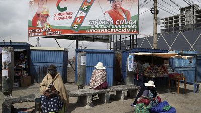 A billboard promoting presidential candidate Carlos Mesa of the Citizen Community political party towers over a trio of women in Rio Seco, Bolivia, Saturday, Oct. 17, 2020