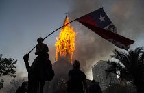 Un manifestante enarbola una bandera de Chile frente a la cúpula de la Asunción en llamas
