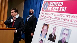 A poster showing six wanted Russian military intelligence officers is displayed as Assistant Attorney General for the National Security Division John Demers, speaks.