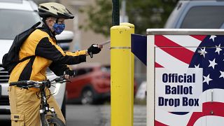 Cyclist Mickey McDiarmid votes by dropping her completed ballot into a ballot drop box Monday, Oct. 19, 2020, in Bellingham, Washington.