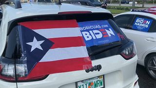 Un vehículo con una bandera de Puerto Rico y el cartel "Boricuas con Biden"