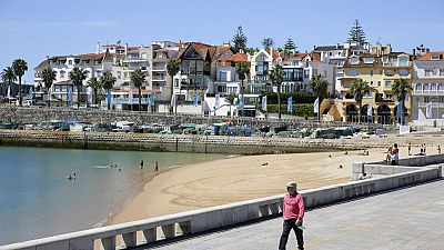 Um homem, com uma máscara de proteção contra o coronavírus na mão, caminha junto à praia quase vazia de Cascais, nos arredores de Lisboa, na sexta-feira, 22 de maio de 2020. 