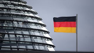 A flag of Germany waves next to the dome of the Reichstag building where the German federal parliament Bundestag meets.
