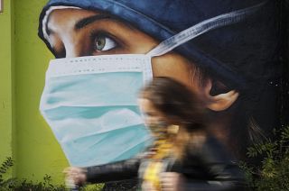 A woman walks in from of a mural painting of a nurse, in Milan, Italy, Wednesday, Oct. 14, 2020.