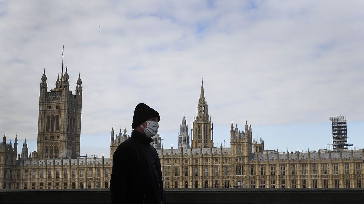 A man wears a face mask as he passes Britain's Parliament in London, Friday, Oct. 16, 2020. 