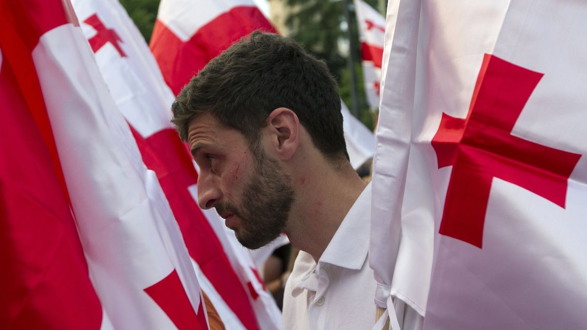 An opposition demonstrator stands between Georgian flags during a rally in front of the Georgian Parliament's building in Tbilisi, Georgia, Saturday, July 6, 2019.