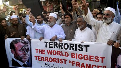 Pakistan traders hold a banner with a defaced picture of French President Emmanuel Macron during a protest against the publishing of caricatures of the Prophet Muhammad.