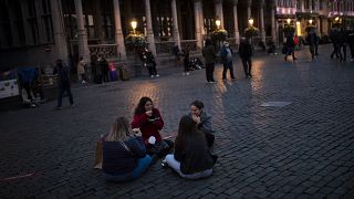 Students sit and eat waffles on Grand Place during an autumn evening prior to the curfew in downtown Brussels, Oct. 23, 2020.