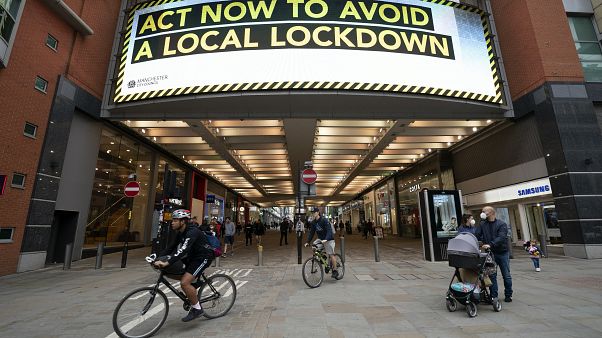 Members of the public are seen by a public information message in Manchester, England. Members of the public are seen by a public information message in Manchester, England.