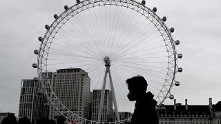 A man wears a face mask as he passes the London Eye in London, Thursday, Oct. 29, 2020